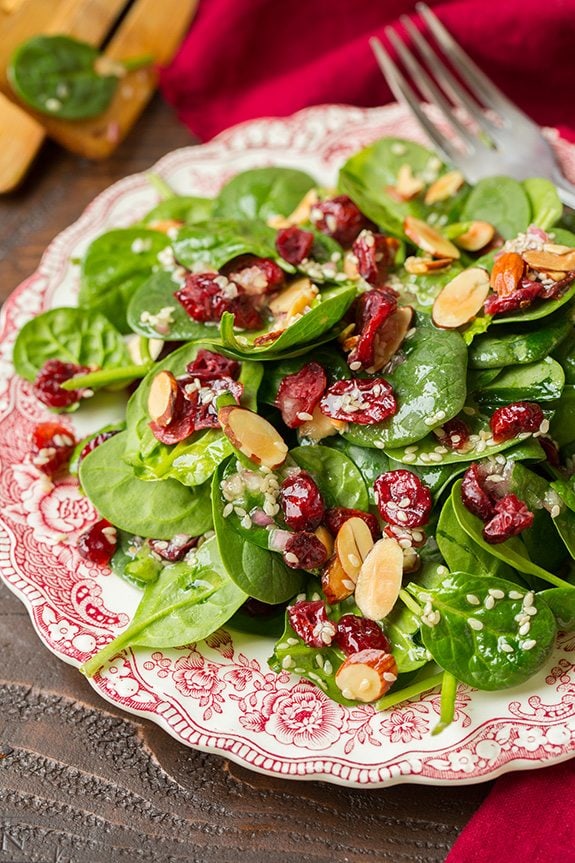 Spinach salad on a vintage red and white plate layered with dried cranberries, sliced almonds and a sesame seed dressing.