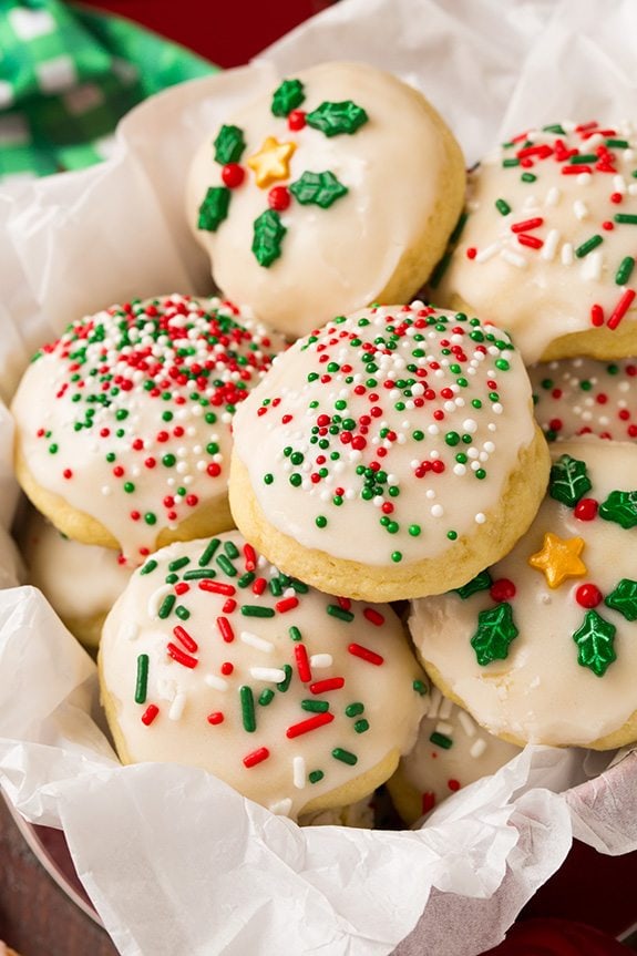 Italian Ricotta Cookies in a gift tin with tissue paper. They are decorated with glaze and Christmas sprinkles.