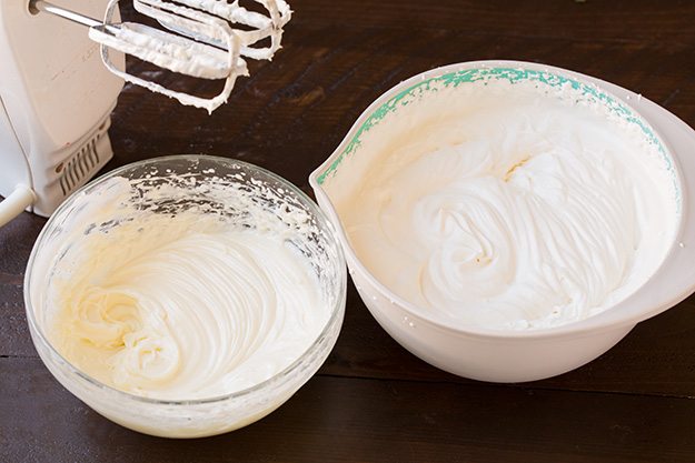 whipped cream in two mixing bowls next to electric mixer