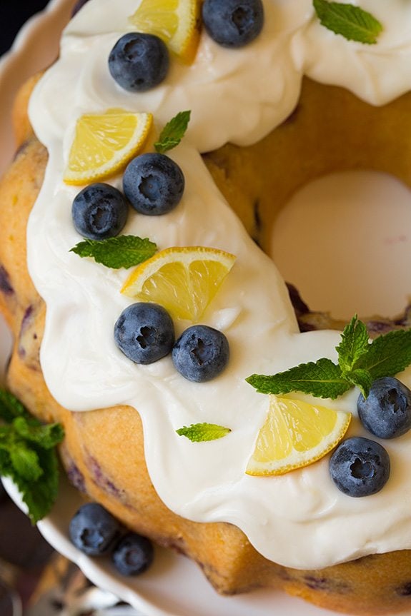 close up of Lemon Blueberry Bundt Cake with cream cheese icing topped with blueberries, mint leaves and lemon slices