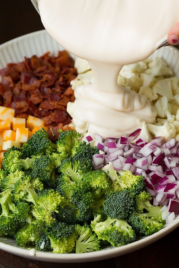 Broccoli and Cauliflower Salad ingredients in a white bowl with the dressing getting poured over the top
