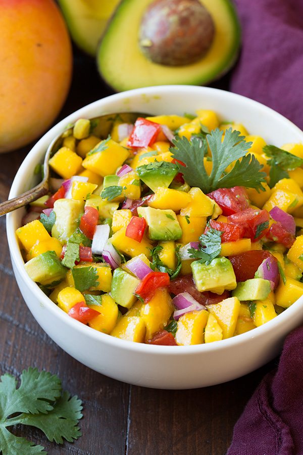 Mango Avocado Salsa in a white serving bowl, set over a wooden table surface.