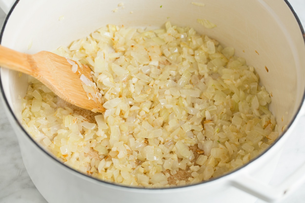 Sautéing onion and garlic in a large white pot.