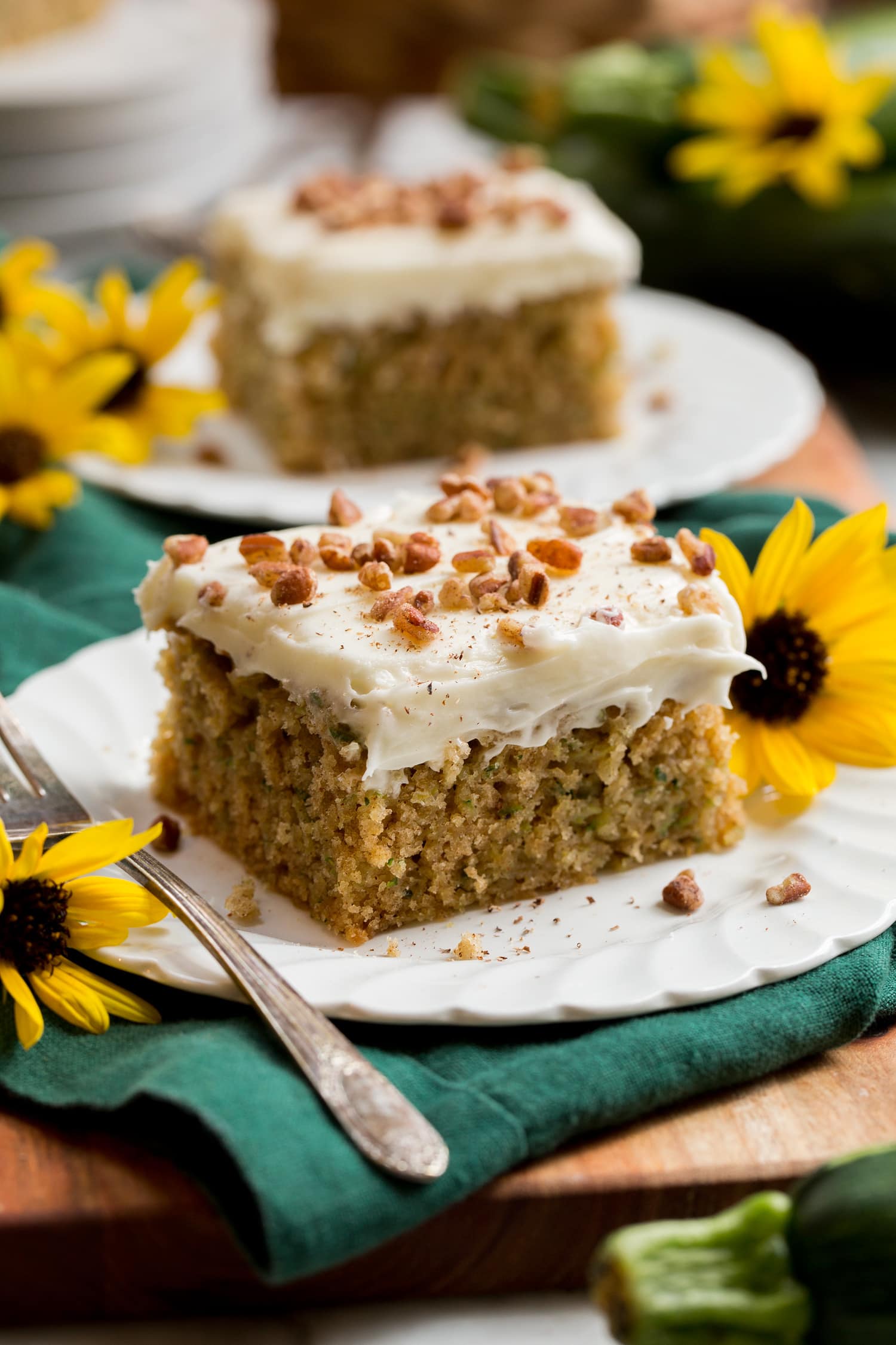Two slices of homemade zucchini cake with cream cheese frosting with sunflowers decorating plates.