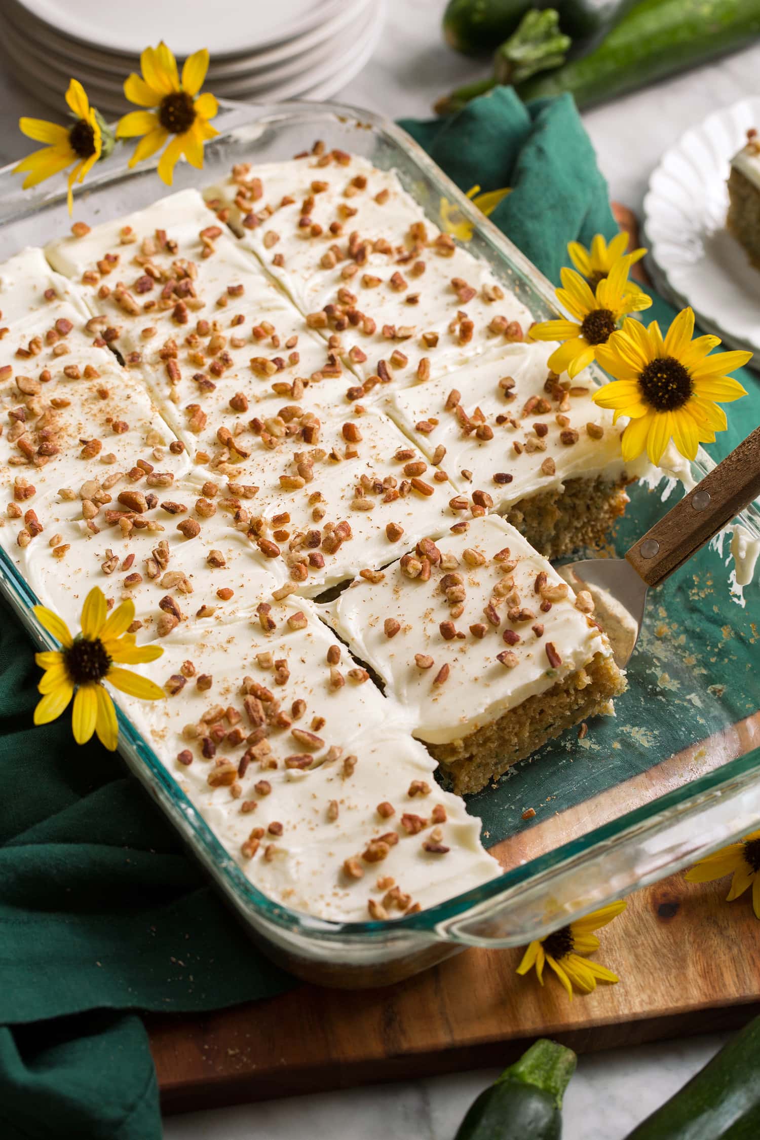 Glass baking pan with homemade zucchini cake topped with cream cheese frosting and chopped pecans.