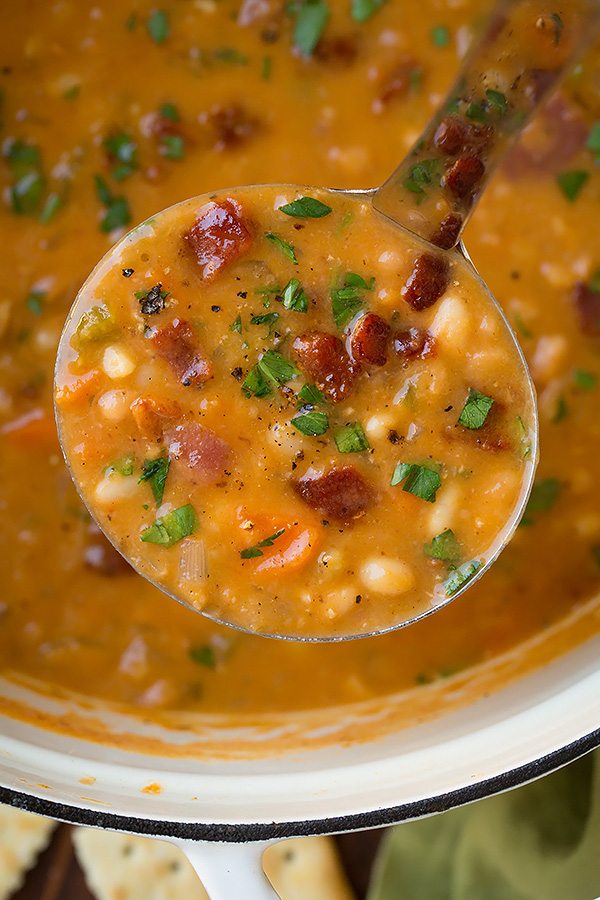Close up image of a ladle filled with bean and bacon soup.