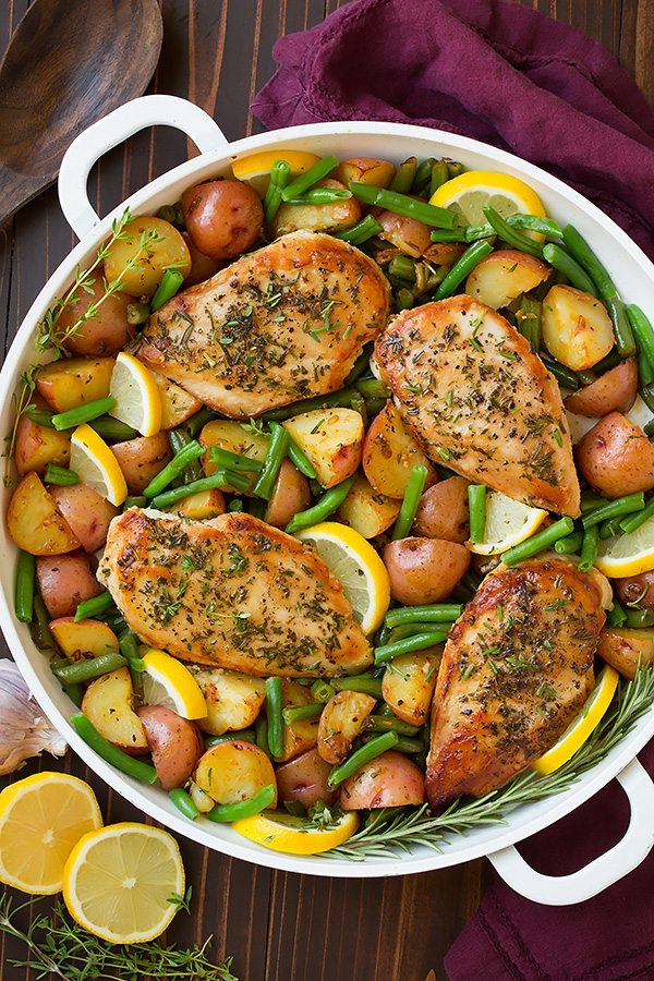 Garlic and herb seasoned chicken breasts in a skillet with green beans, potatoes and lemons.