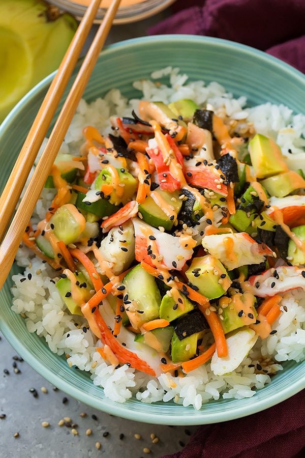 California roll ingredients layered bowl, including sushi rice, crab, nori, carrots, cucumber, avocado, spicy mayo and sesame seeds.