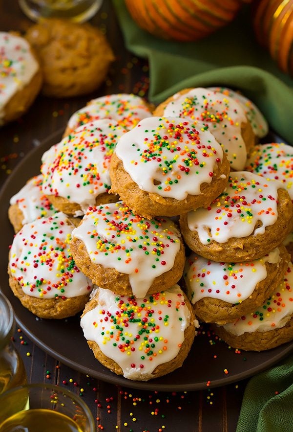 Stack of soft pumpkin cookies with a vanilla icing and fall sprinkles set on a brown serving plate.
