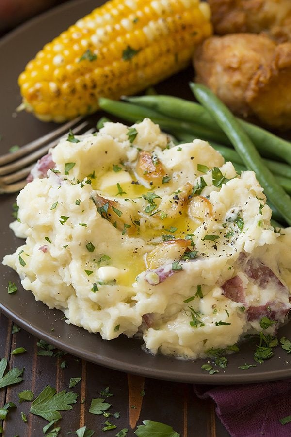 Serving of garlic mashed potatoes on a matte brown serving plate with a side of green beans, chicken and corn.