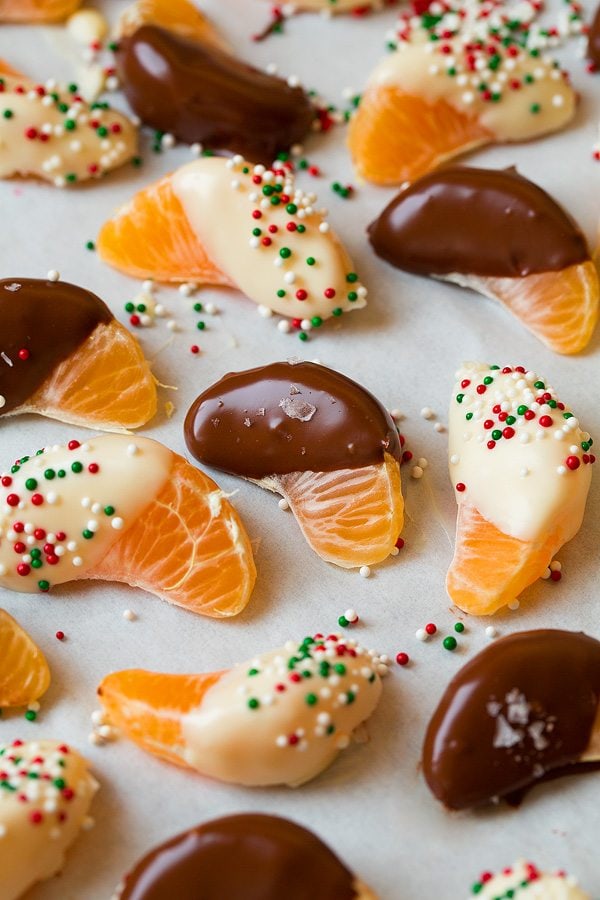 Chocolate dipped mandarin oranges on parchment paper, some are covered with Christmas sprinkles or sea salt.