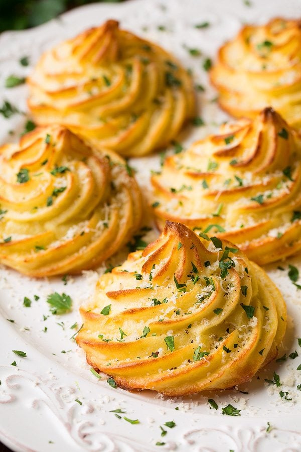 Five Duchess Potatoes shown on a white serving plate, garnished with parsley and parmesan cheese.