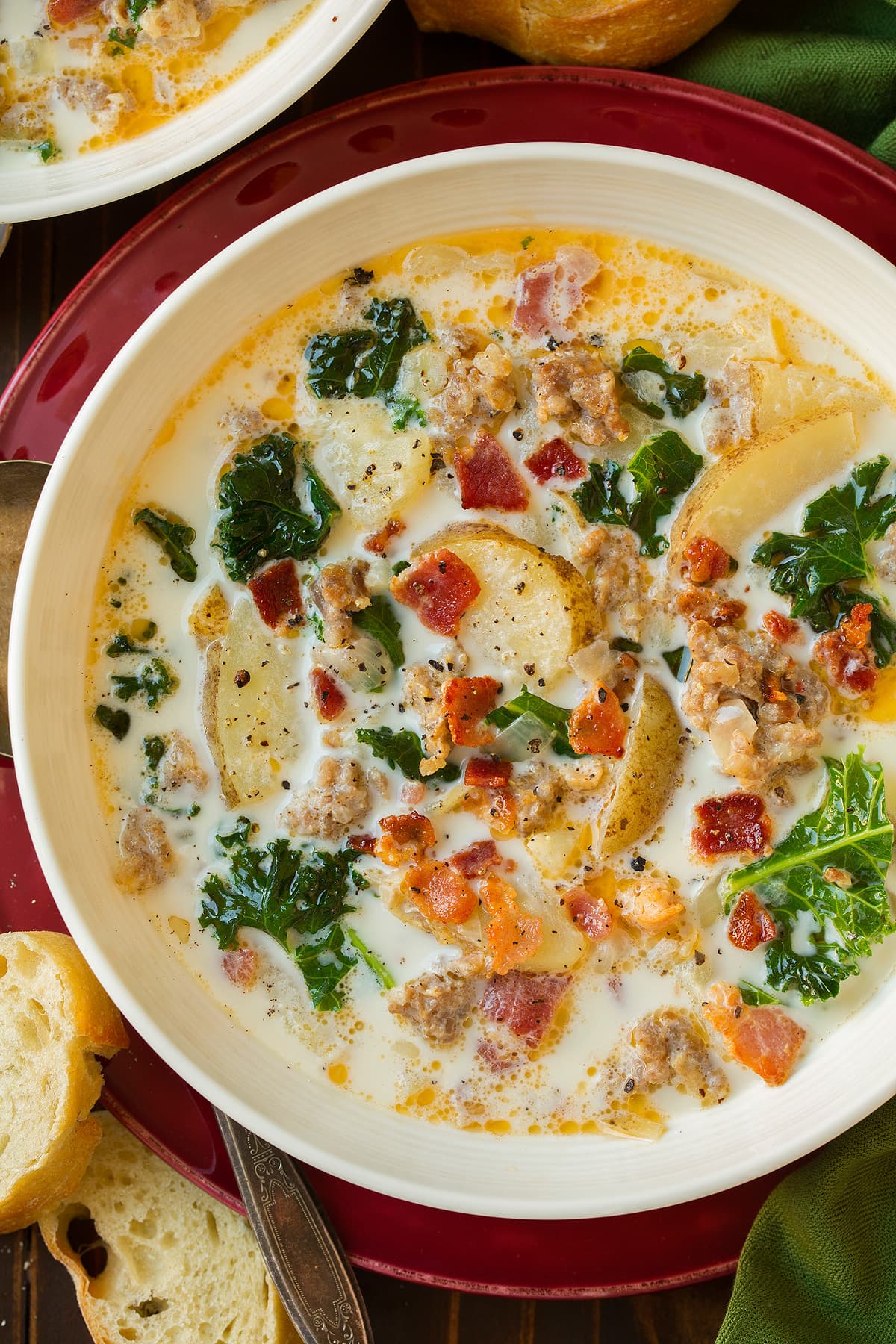 Zuppa Toscana soup in a white single serve bowl set over a red plate.