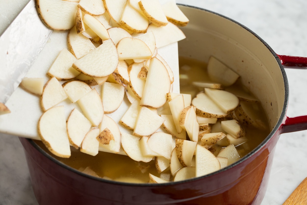 Adding thinly sliced potatoes to mixture in a large pot for zuppa toscana.