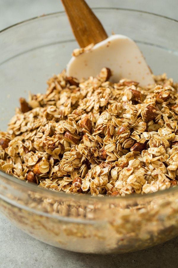 Mixing granola in a glass bowl. Mixture includes, oats, flax seeds, almonds, honey, brown sugar, almond and vanilla extract, coconut oil.