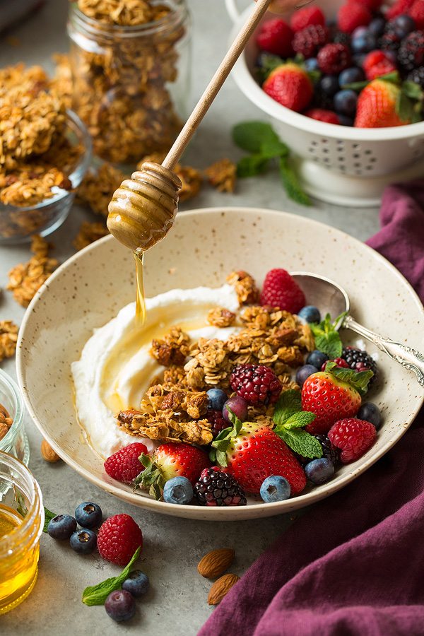 Drizzling honey over granola, fruit and yogurt in a bowl.