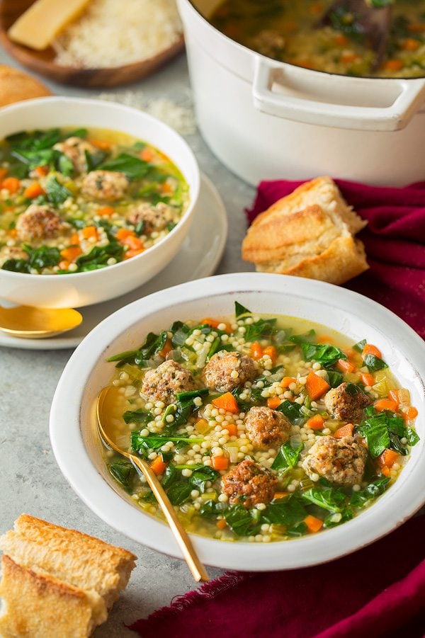Italian Wedding Soup. Two servings shown in a white bowl with a white pot half full in the background.