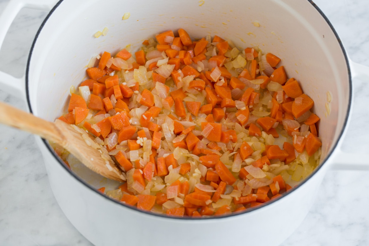 Showing how to make lentil soup. Sautéing diced carrots and onions in a cast iron pot.
