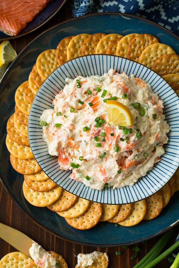 Smoked Salmon Dip in a blue and white striped bowl set over a dark blue plate. Bowl is surrounded by a circle of crackers.