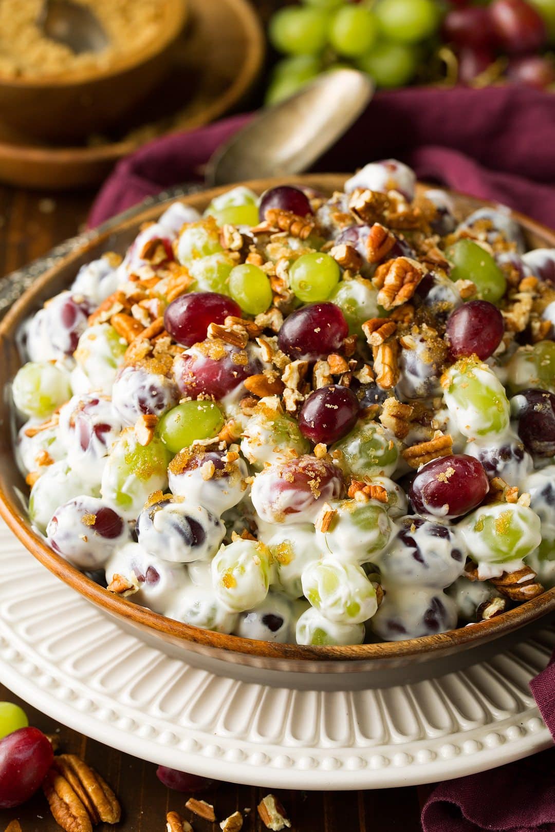 Grape salad toss with a cream cheese dressing and pecans. Served in a wooden bowl over a white scalloped plate.