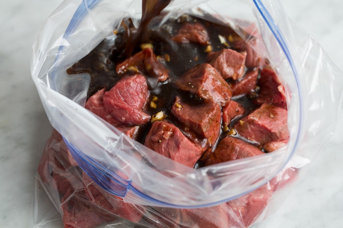Pouring marinade over steak cubes in a bag.