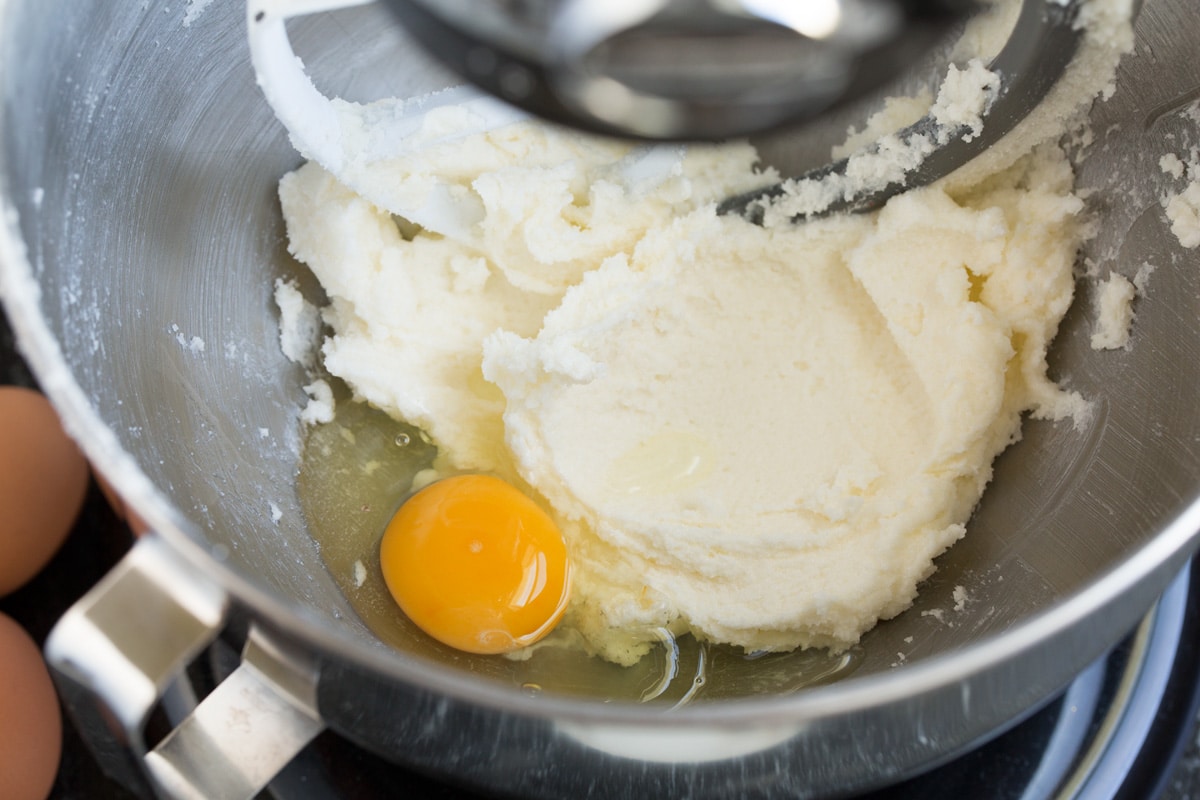 Adding egg to butter sugar mixture in mixing bowl.