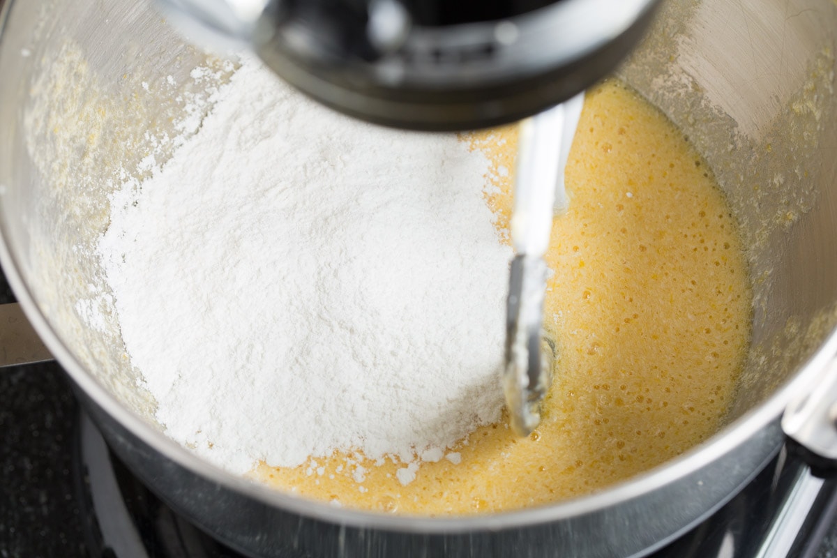 Mixing flour mixture into sugar and egg mixture in mixer bowl.