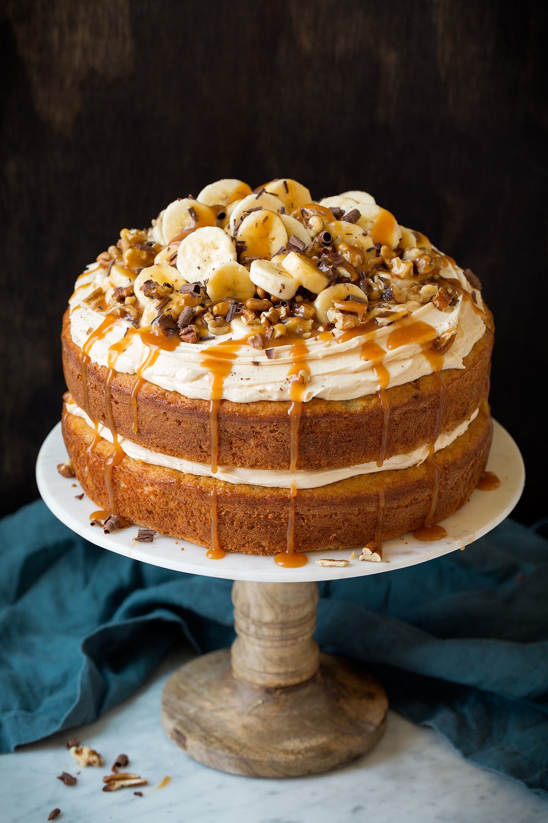A whole banana cake on a marble and wooden cake stand.