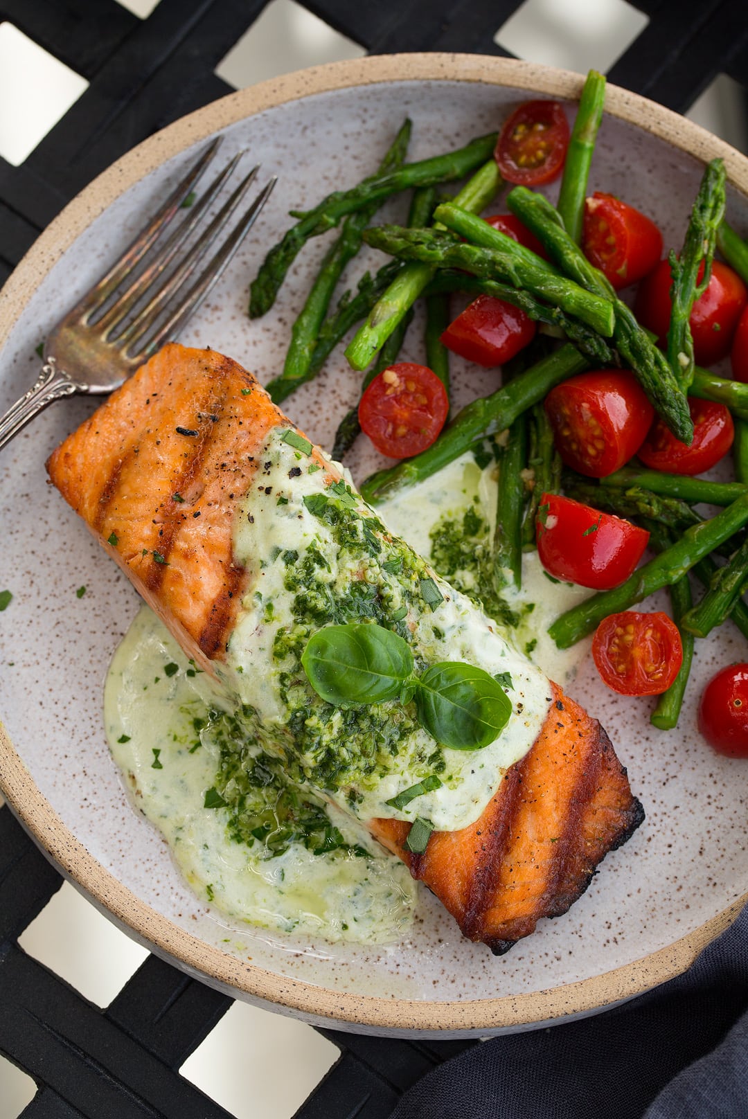 Grilled Salmon fillet with Creamy Pesto sauce on plate with tomatoes and asparagus