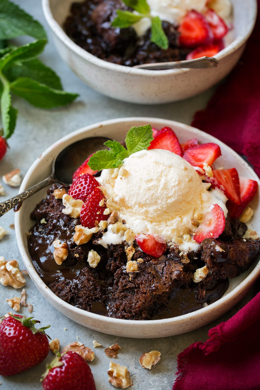 Chocolate cobbler in a white individual bowl topped with vanilla ice cream, strawberries and walnuts.