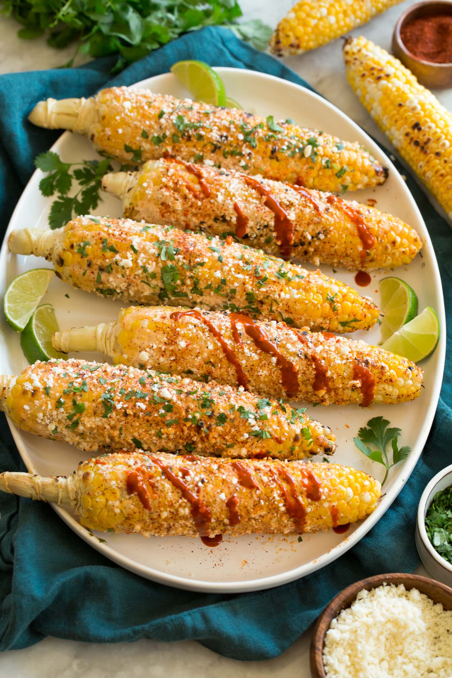 Row of grilled Mexican street corn on a platter with toppings.
