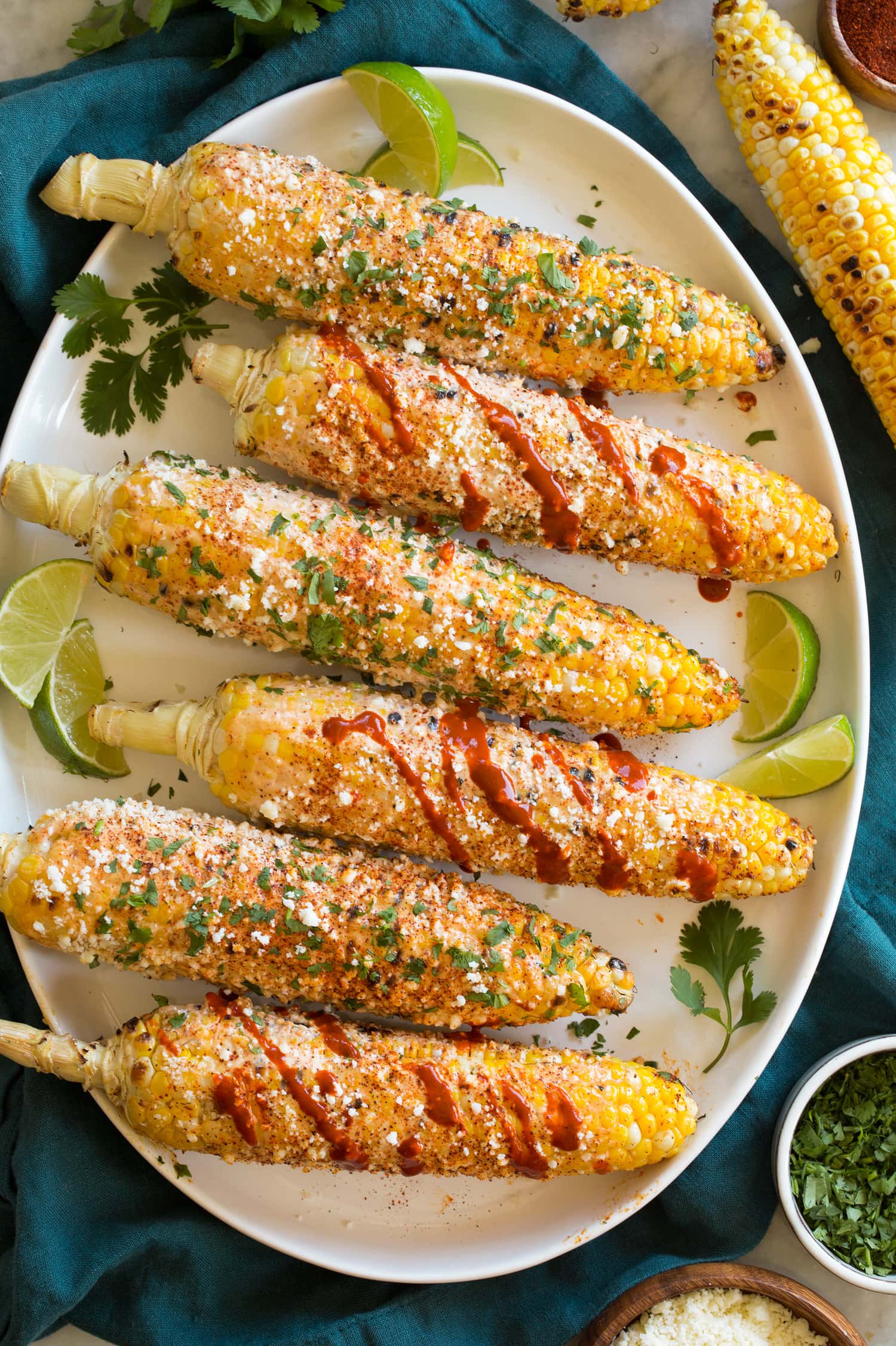Overhead image of grilled Mexican street corn on white oval platter.