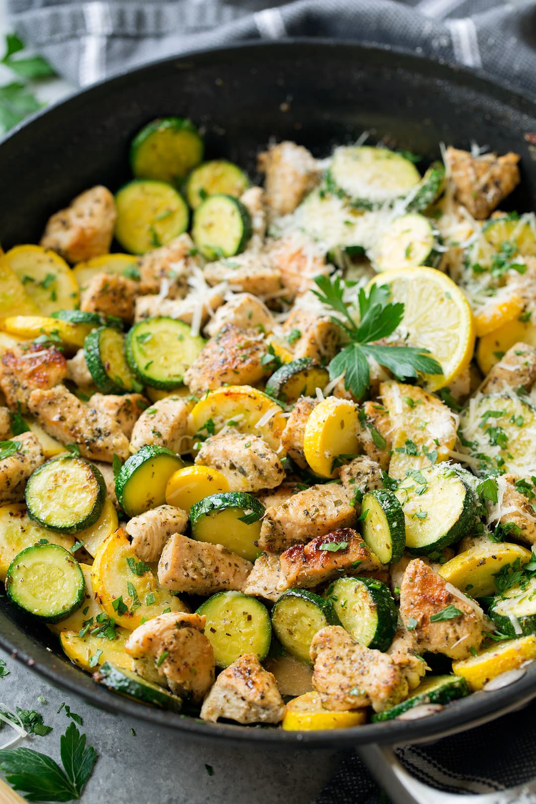 lemon parmesan chicken in skillet with sliced zucchini and squash garnished with parsley