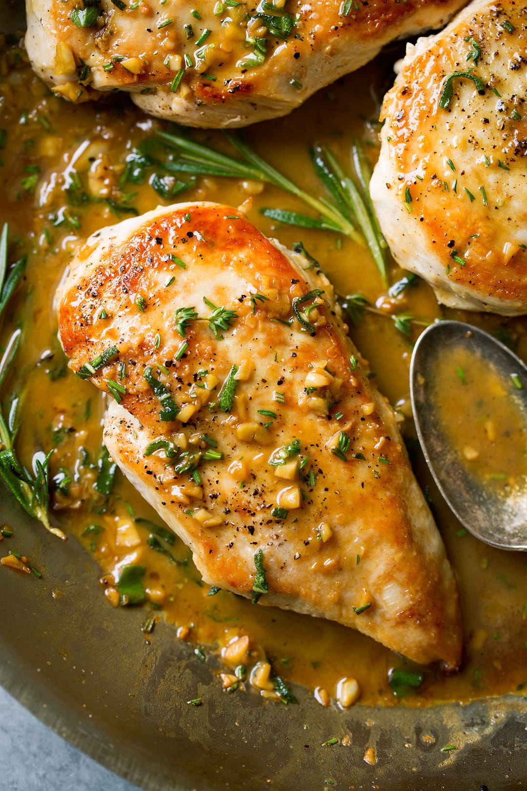 A close up of Skillet Chicken with Garlic Herb Butter Sauce in a pan with herbs and a spoon at the side