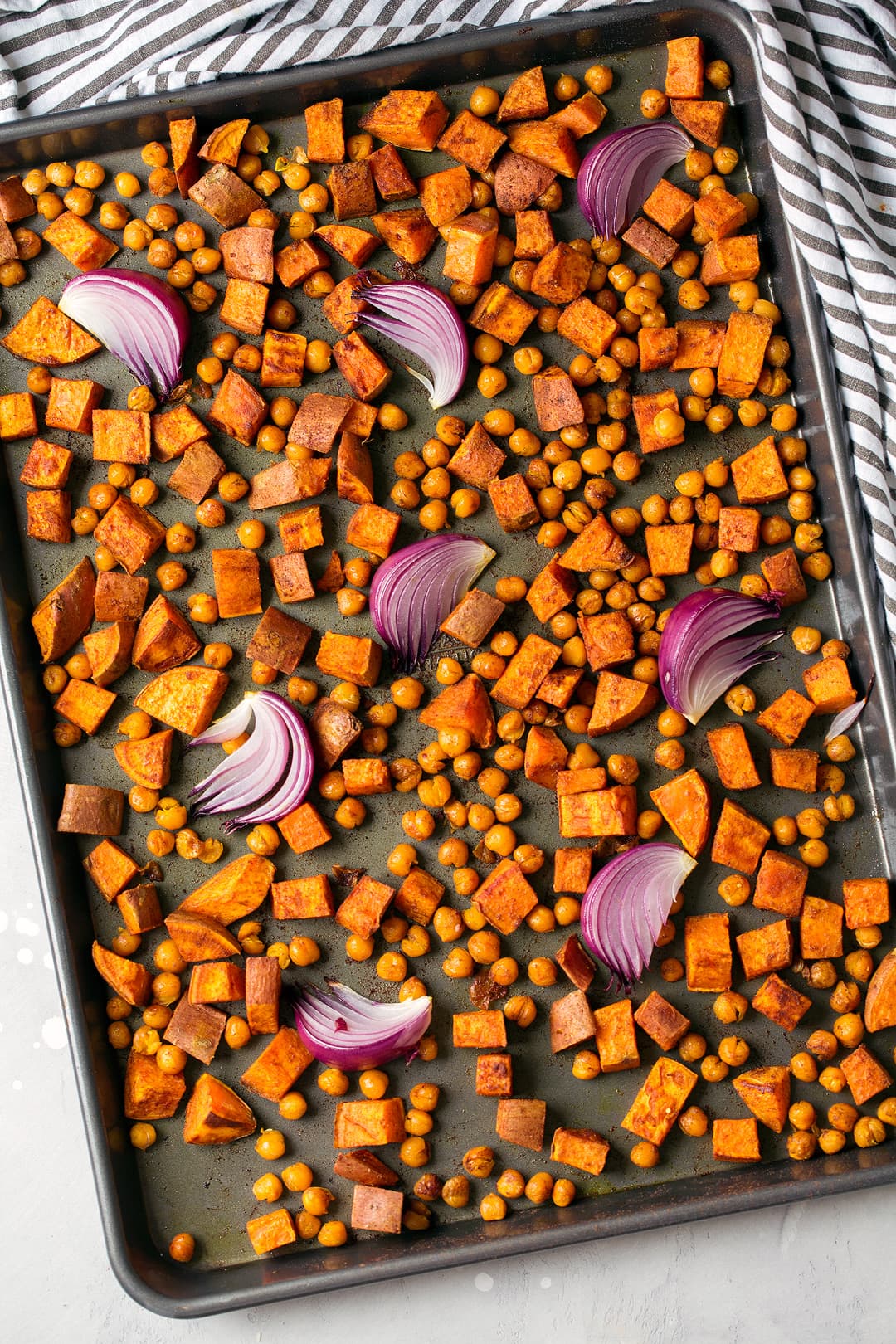 Seasoned sweet potatoes and red onions on baking sheet for buddha bowls.