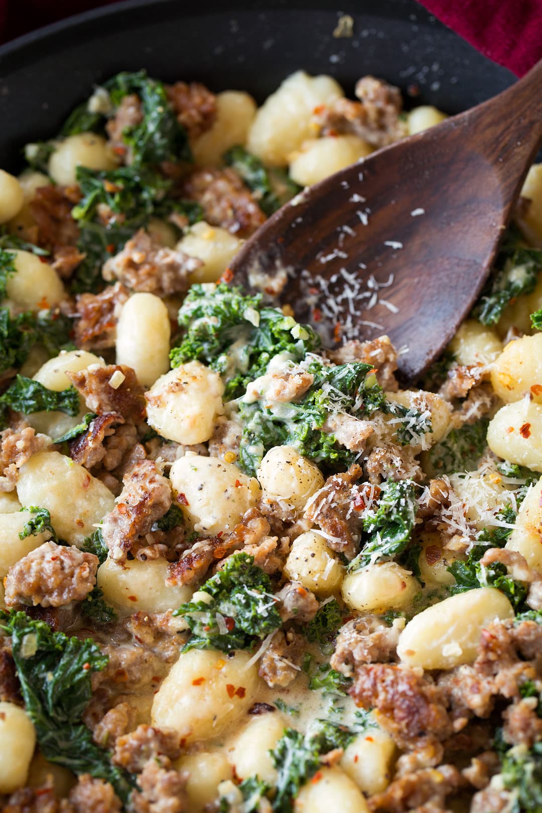 Gnocchi recipe with Italian sausage and kale shown here in a skillet with a wooden spoon for serving.