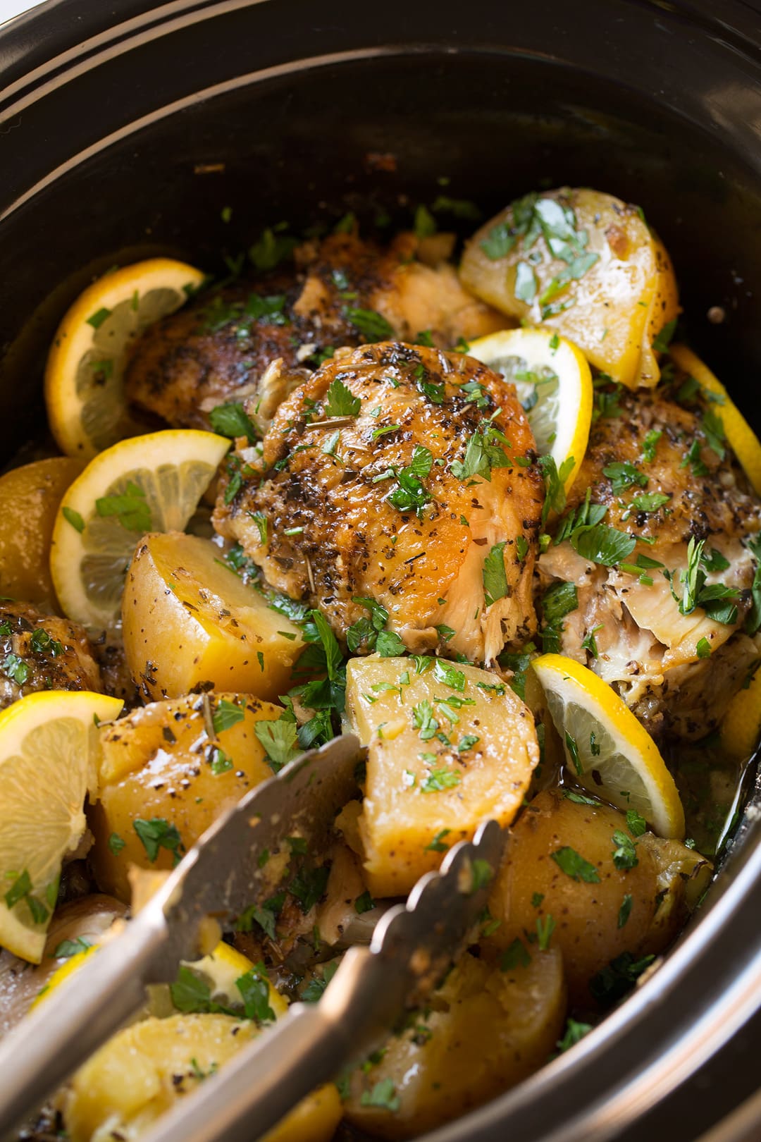 grabbing Slow Cooker Lemon Chicken and Potatoes with a pair of tongs