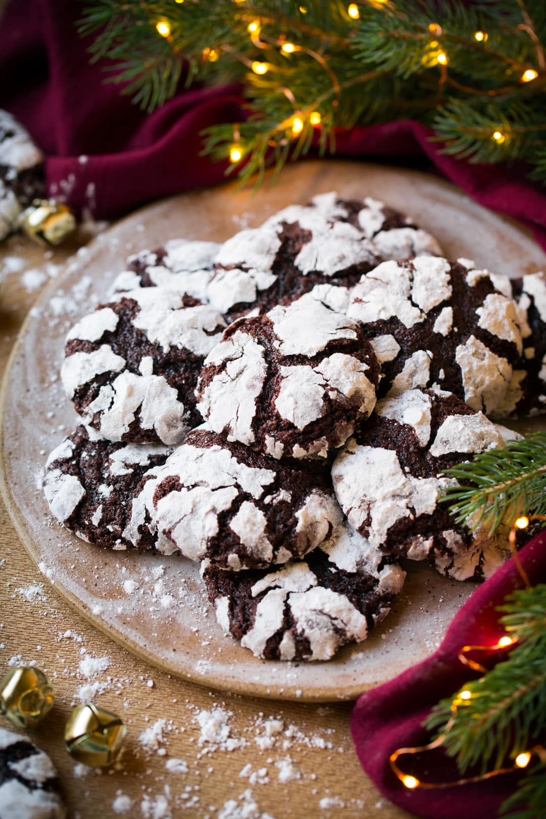 Chocolate Crinkle Cookies shown on a plate by a lit Christmas tree and red napkin.