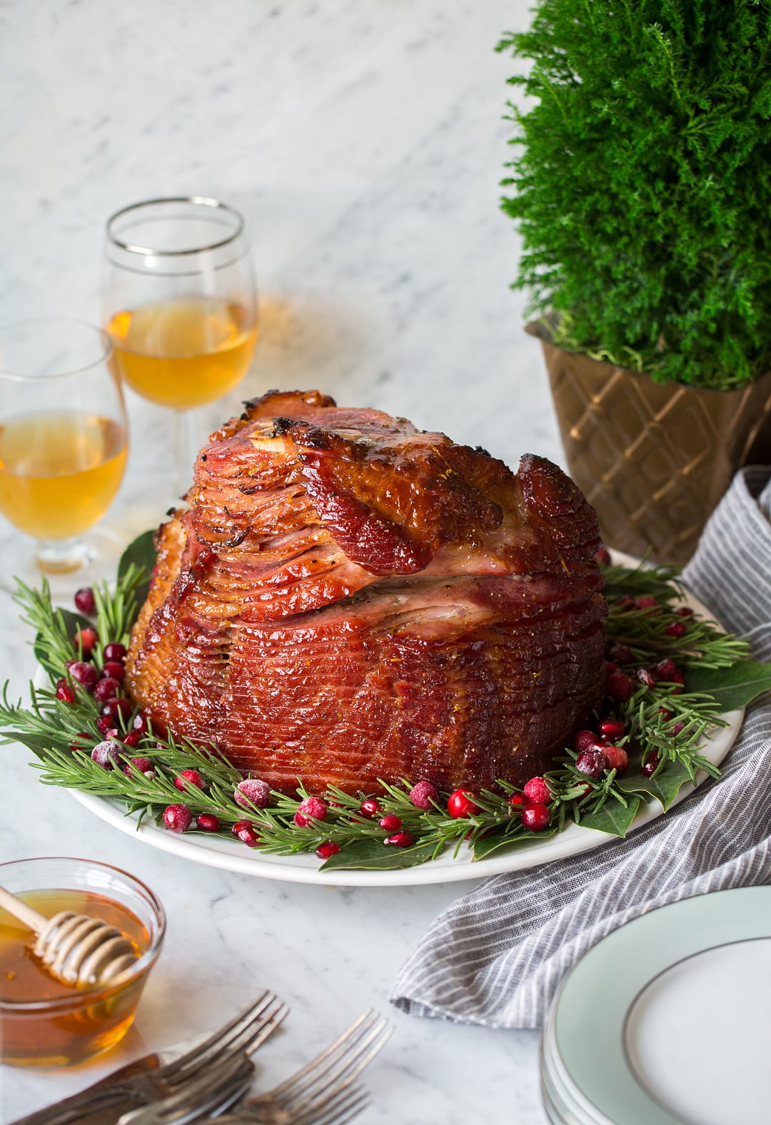 Honey Baked Ham on a serving platter garnished with a wreath of fresh rosemary, bay leaves and cranberries.