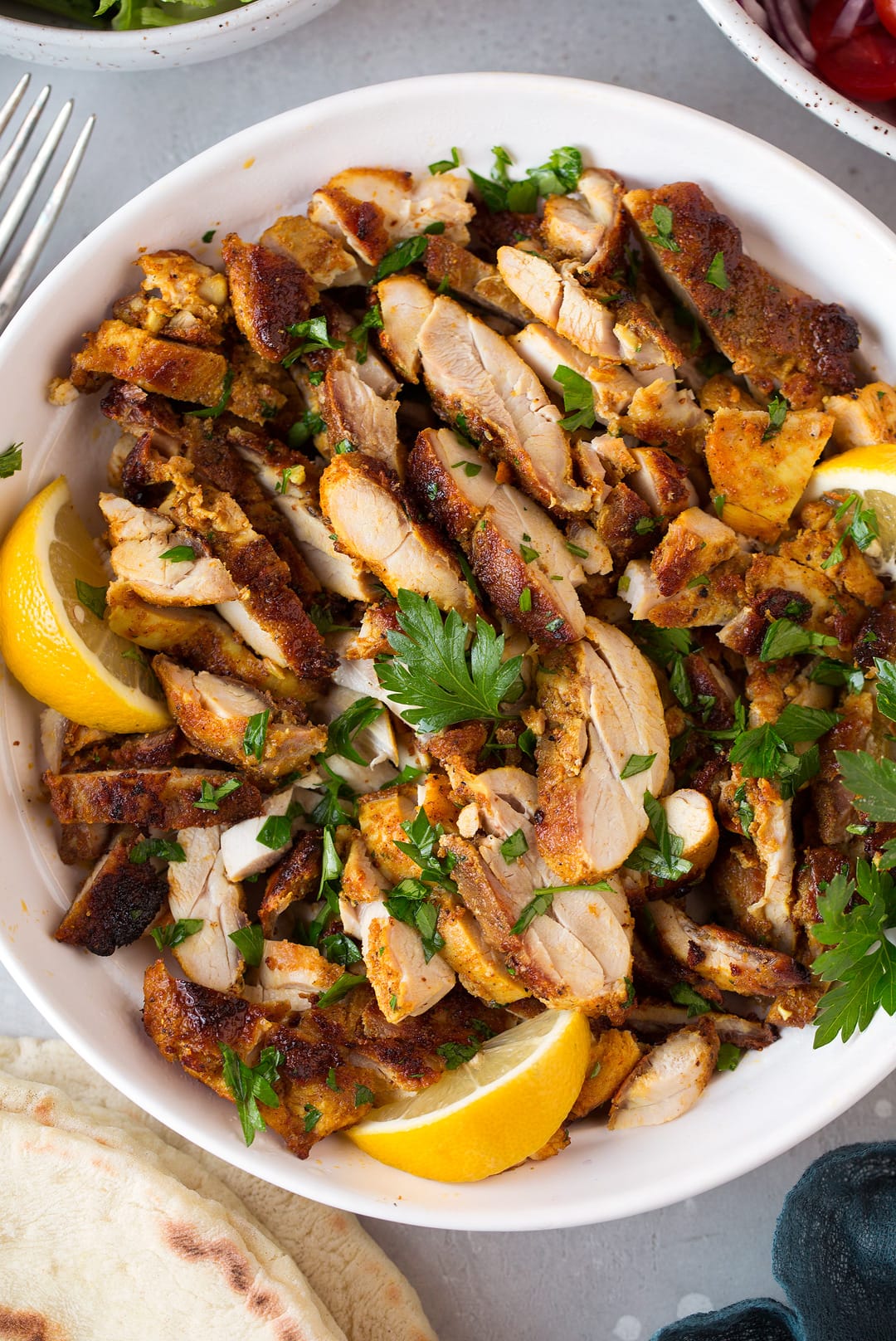 Chicken Shawarma sliced and shown in a serving bowl with lemon wedges and parsley