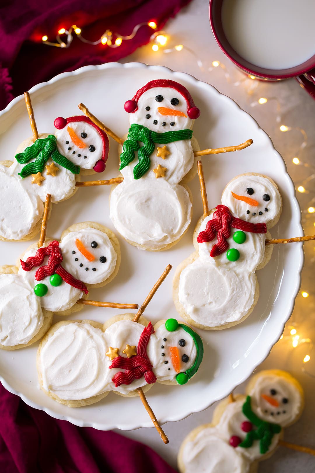 Snowman Sugar Cookies after frosting and decorating. Shown here on a cake plate with Christmas lights around plate.