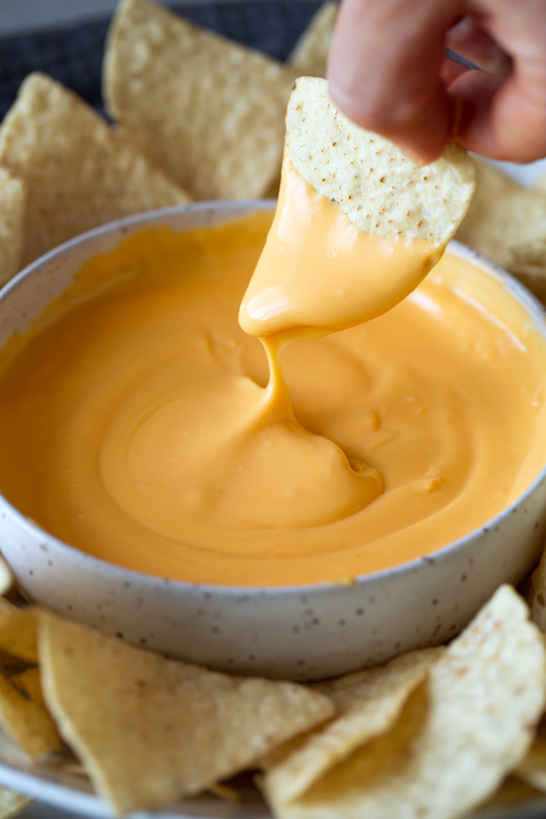 tortilla chip being dunked into a bowl of cheese dip