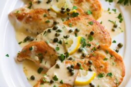 4 servings of chicken piccata on a white oval serving platter.