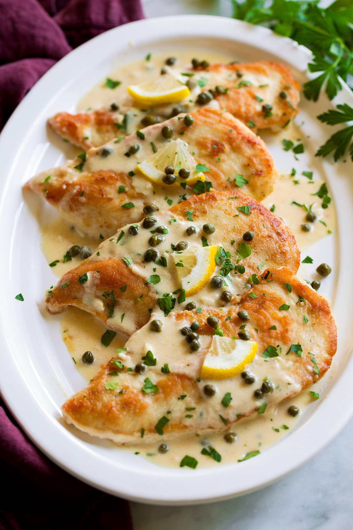 4 servings of chicken piccata on a white oval serving platter.