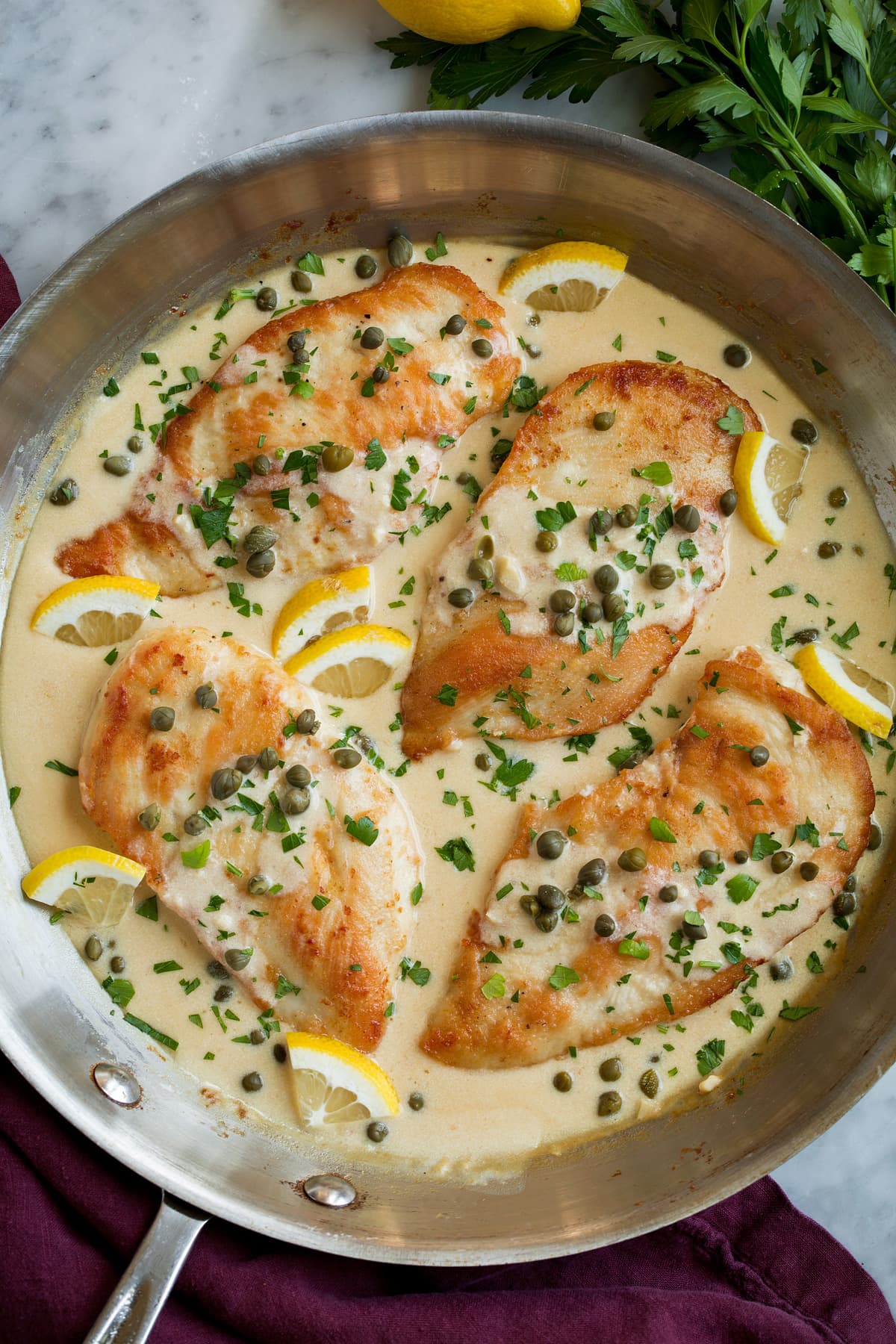 Four servings of chicken piccata in a creamy lemon piccata sauce, shown after cooking in a large aluminum skillet.