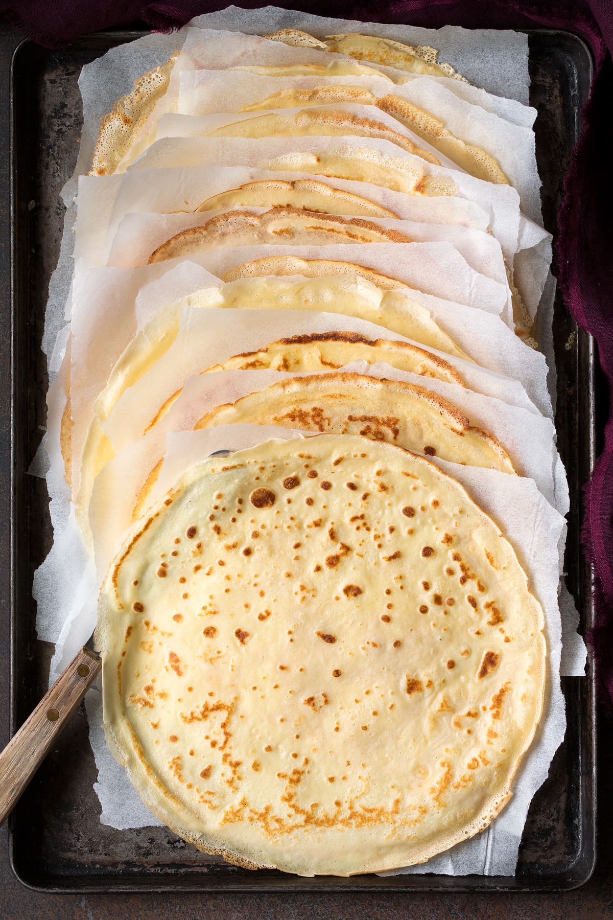 Crepes made from scratch, shown after cooking on a baking sheet with parchment paper between each. 
