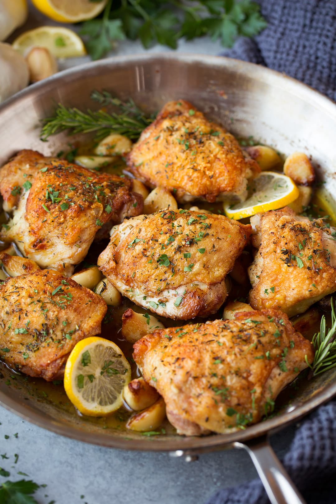 Six pieces of golden brown crispy chicken thighs shown here in a skillet after roasting with garlic and herbs.