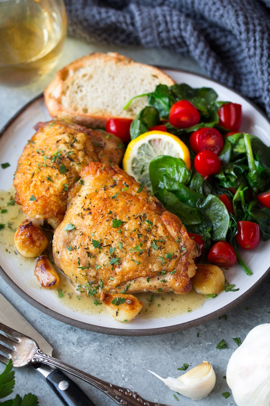 Roast chicken with garlic shown in on a single serve plate with pan sauce, along with a side salad, and fresh bread.
