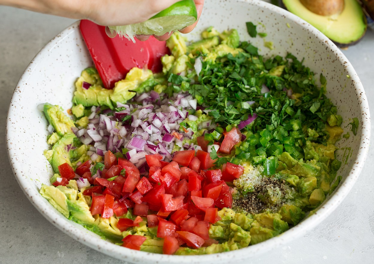 Adding diced tomatoes, red onion, cilantro, garlic, jalapeño and lime juice to mashed avocado in mixing bowl.