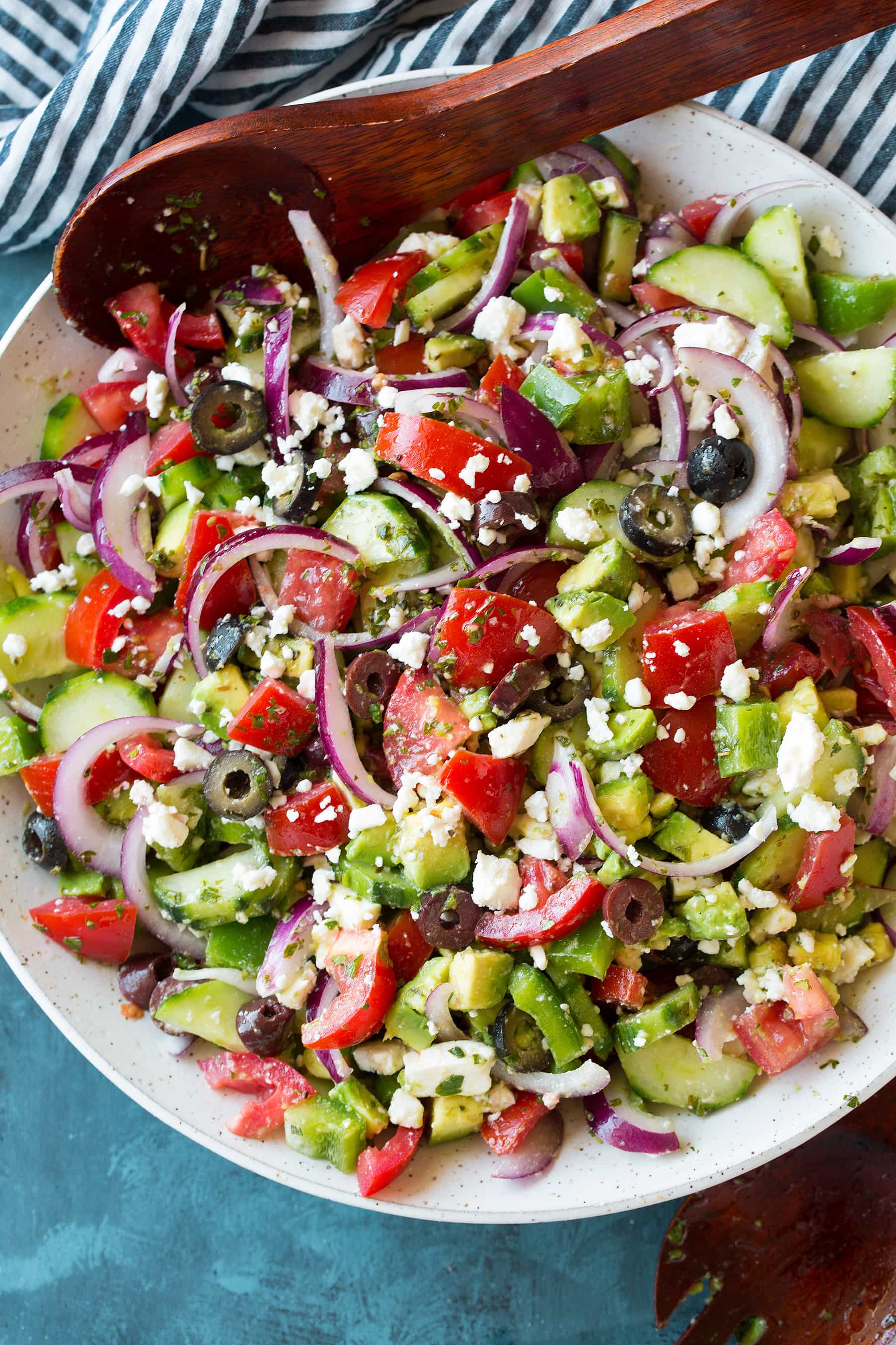 An overhead shot of a Greek Salad in a white bowl with salad servers